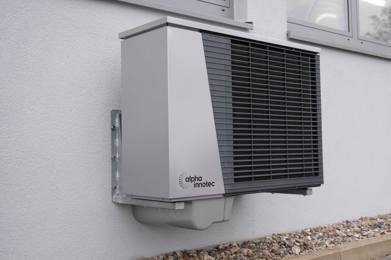 Ein modernes Wärmepumpengerät von Alpha Innotec mit fortschrittlicher Heizungstechnik ist an einer Außenwand über dem felsigen Boden unter den Fenstern montiert